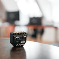 Two compact black Shelly 2PM Gen3 x2 devices with labeled terminals and wiring diagrams rest on a dark wooden surface, with a blurred indoor background.