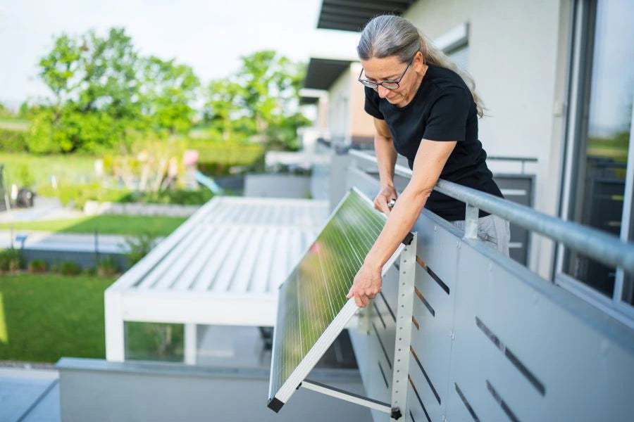 Woman adjusts a solar panel on her balcony – Shelly balcony power plant helps precisely measure kilowatt hours for ROI calculation
