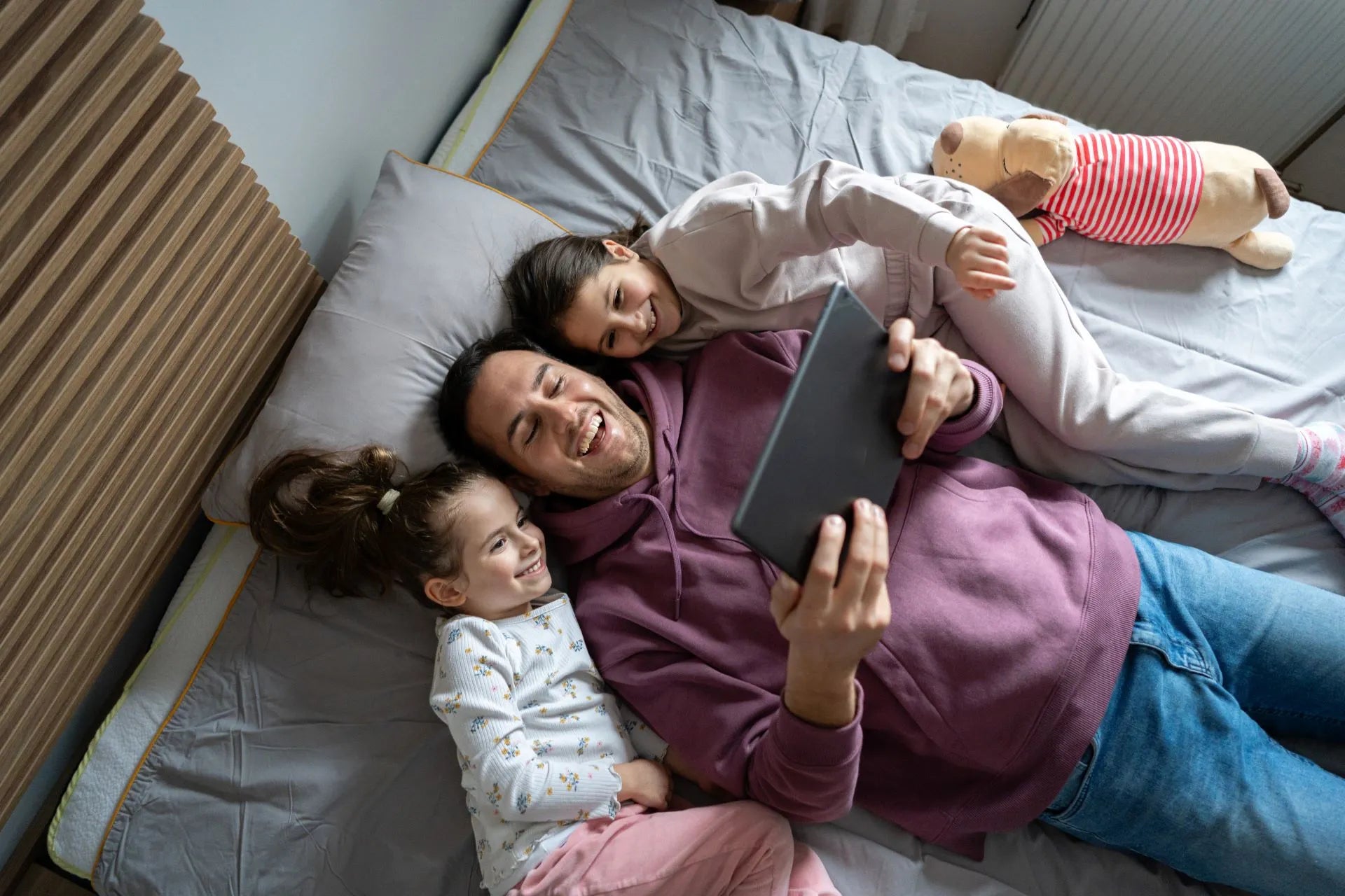 Father and daughters in bed with an iPad, enjoying the comfort of modern building control with KNX and Shelly