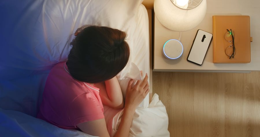woman in bed with smartphone; an Alexa Echo on the nightstand controls Shelly devices by voice command 
